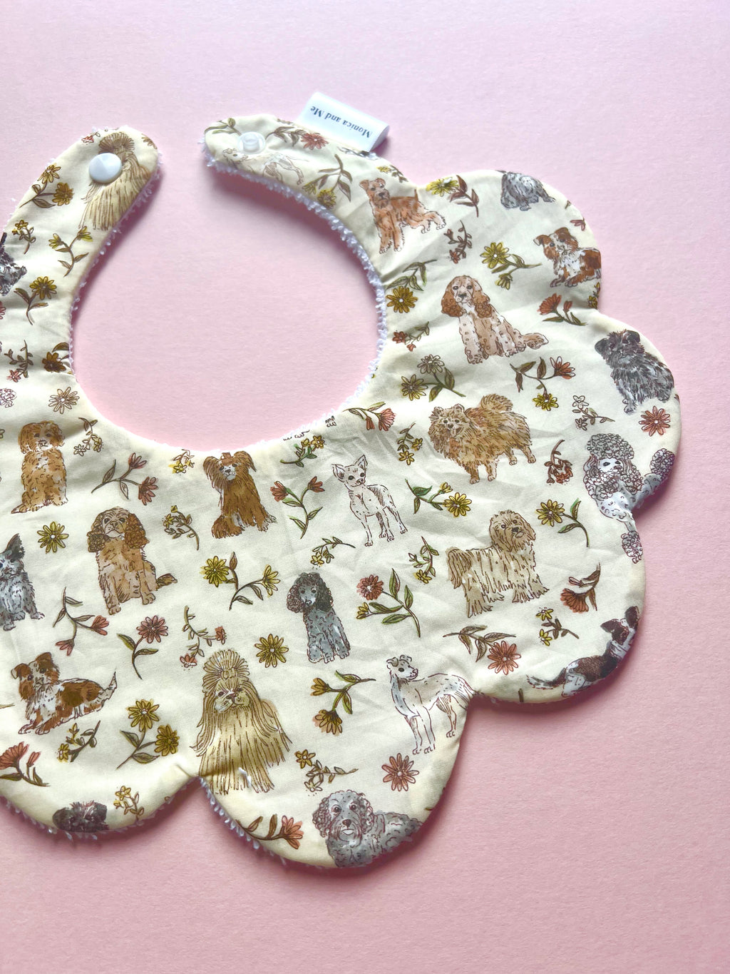 Scalloped baby bib made with Liberty London fabric. The bib features a print with dogs in cream and  grey tones in a cream background. 