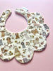 Scalloped baby bib made with Liberty London fabric. The bib features a print with dogs in cream and  grey tones in a cream background. 