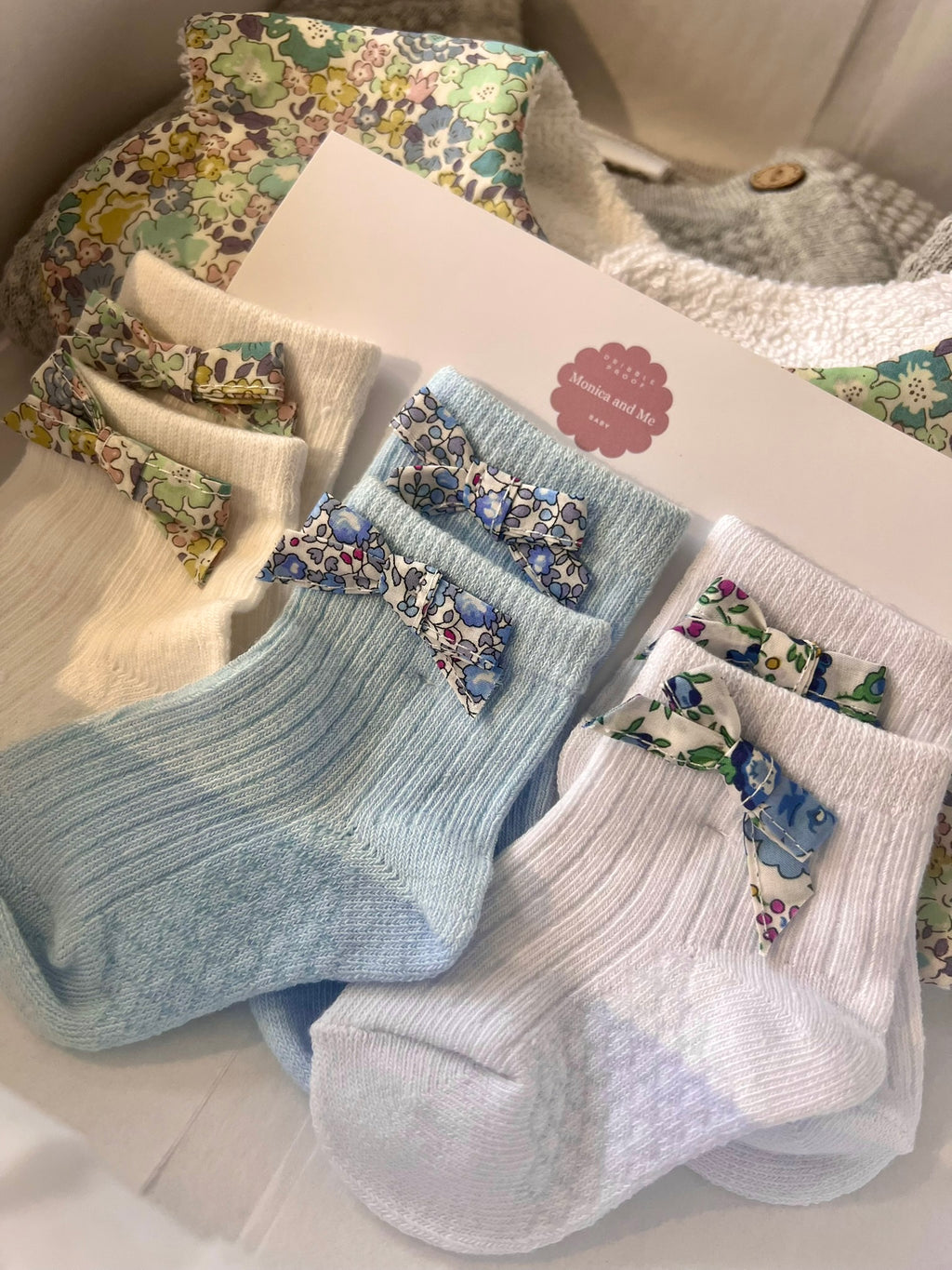 Baby gift box that includes baby socks with Liberty London bows, Scalloped baby bib in Michelle blue print, grey knitted set of top and leggings.