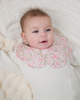 Baby wearing a scalloped baby bib in pink liberty floral.