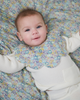 Baby wearing a Liberty floral bib on a floral blanket