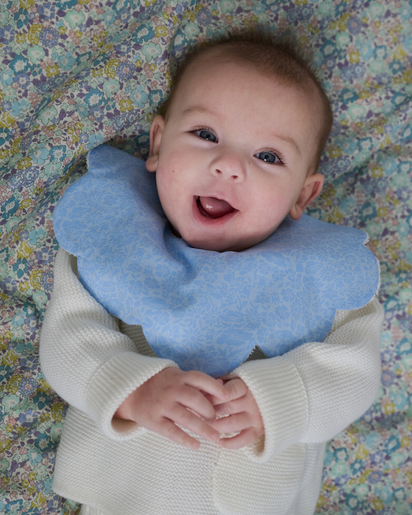 Baby wearing a blue bib on a floral-patterned blanket