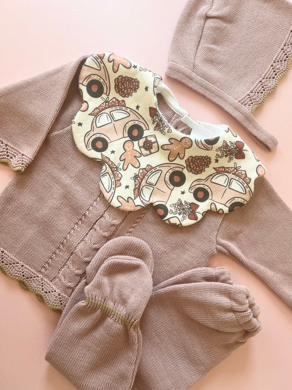 Soft scalloped baby bib in Liberty fabric with whimsical holiday print of cars and gingerbread men, matched with a knitted pink cardigan, bonnet, and mittens. Perfect winter outfit for babies by Monica & Me, bringing together quality and seasonal flair.